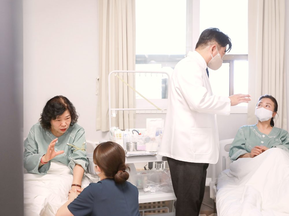 병실에서 원장과 간호사가 췌장암 치료 중인 환자의 눈 흰자위 색과 컨디션을 살피며 이야기를 나누는 모습