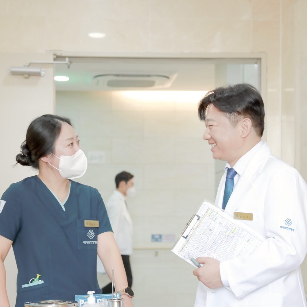 복도에서 간호사와 원장이 입원 환자의 투약 기록지를 들고 웃으며 이야기하는 모습