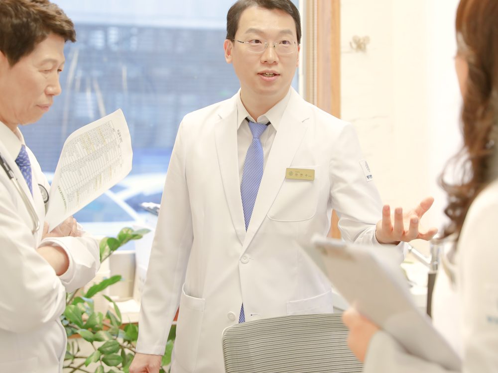 원장이 서류를 든 동료 의료진들에게 새로 입원할 환자의 치료 경과를 설명하는 모습