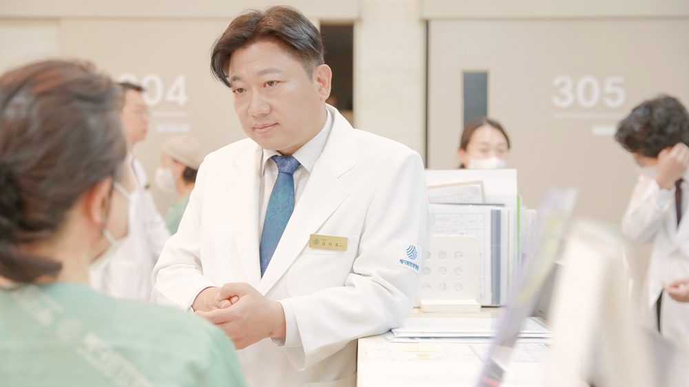 간호사실 앞에서 원장이 환자복을 입은 환자와 마주 서서 최근 검사 결과를 이야기하는 모습